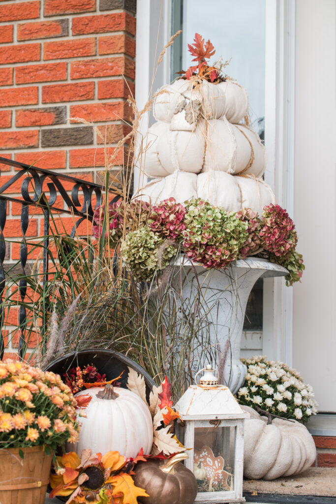 Perennial grasses in terracotta pots on a front step beside orange mums and a white lantern