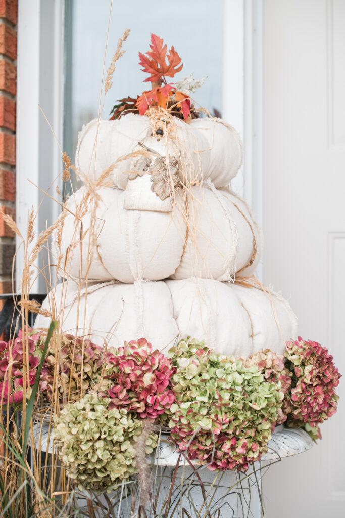 drop-cloth pumpkin topiarie on a front step, one on a white urn with dried hydrangea blooms, beside a white door