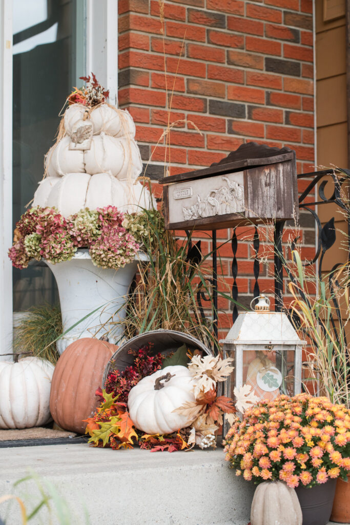 Perennial grasses in terracotta pots on a front step beside orange mums, a mailbox with pumpkins and a white lantern