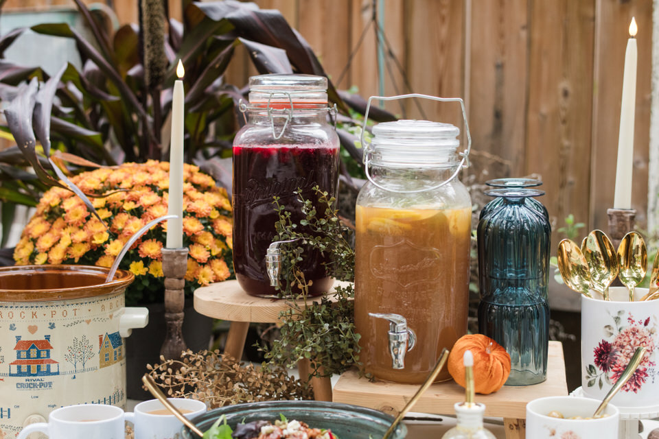 Two glass drink dispensers holding ruby Cranberry Fizz and a Sparkling Pear, Rosemary, and Lemon Refresher