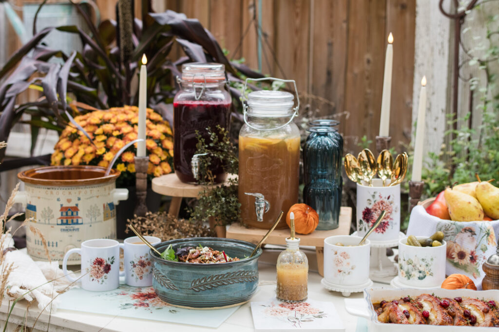 Close-up of buffet beverage dispensers on wooden risers and cake stands beside pumpkins and autumn flowers