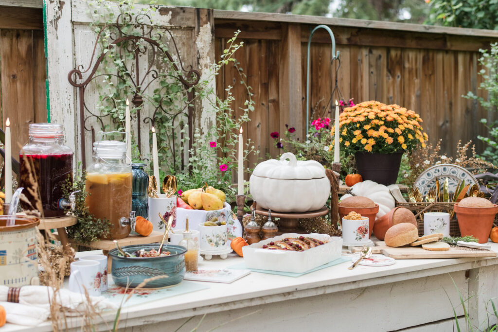 Garden buffet built across a raised lettuce bed with mums, pumpkins, grasses, and burgundy foliage surrounding the dishes