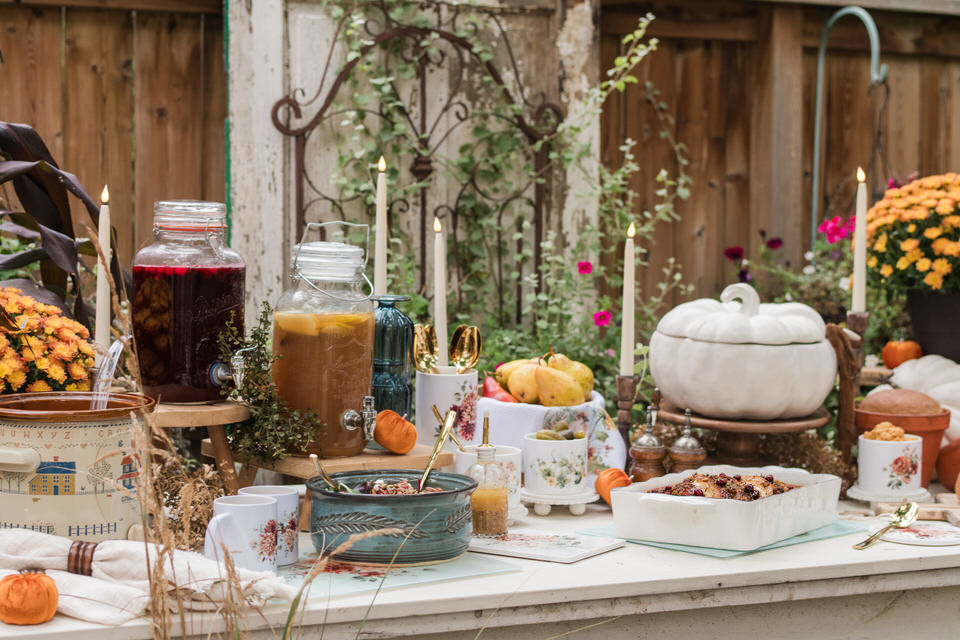 Autumn buffet with a pork tenderloin, a white pumpkin tureen on a wooden pedestal, a harvest salad, olives and pickles in small canisters, and fresh pears