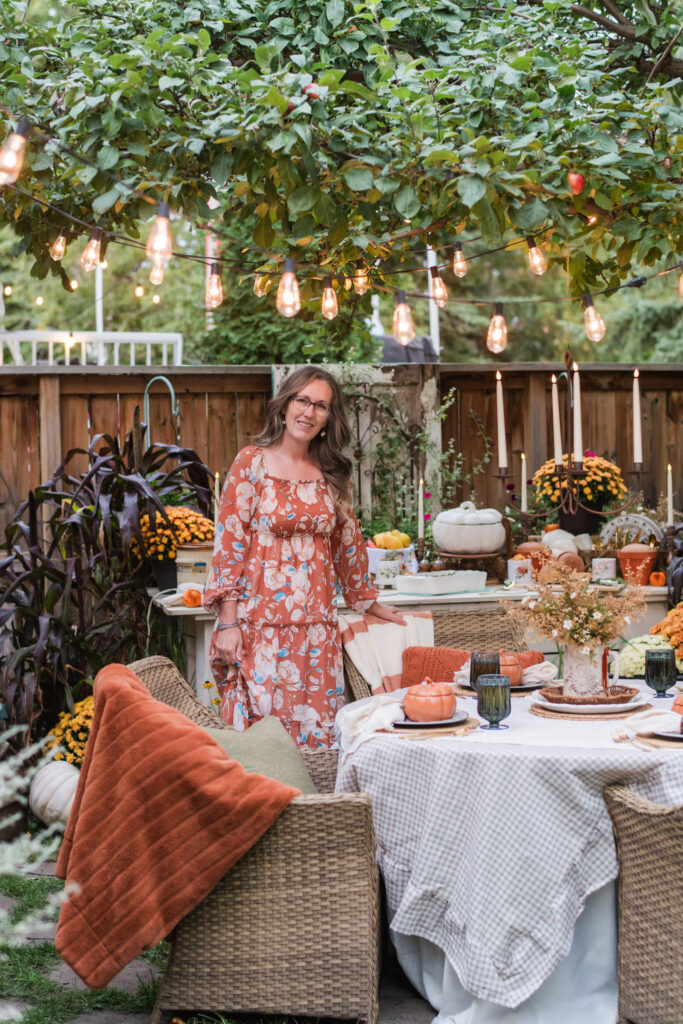 Kimberly standing beneath Edison string lights beside an outdoor dinner table in the evening