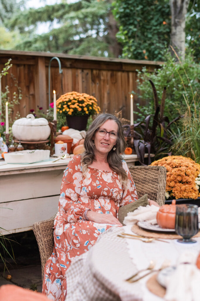 Kimberly sitting in a chair at an outdoor autumn dinner table, looking at the camera