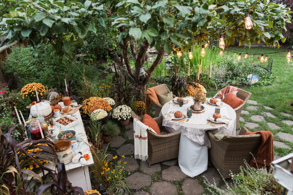 Autumn harvest gathering under an apple tree with a round table, a garden buffet, and string lights overhead