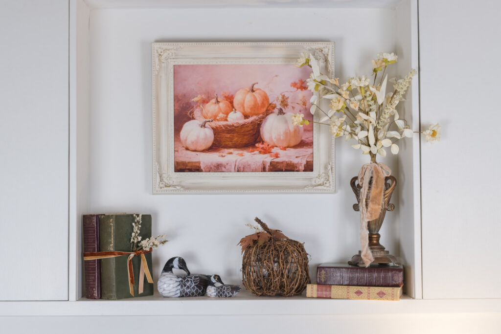 Built-in shelves styled for fall with old books tied in velvet ribbon, a twig pumpkin, and geese