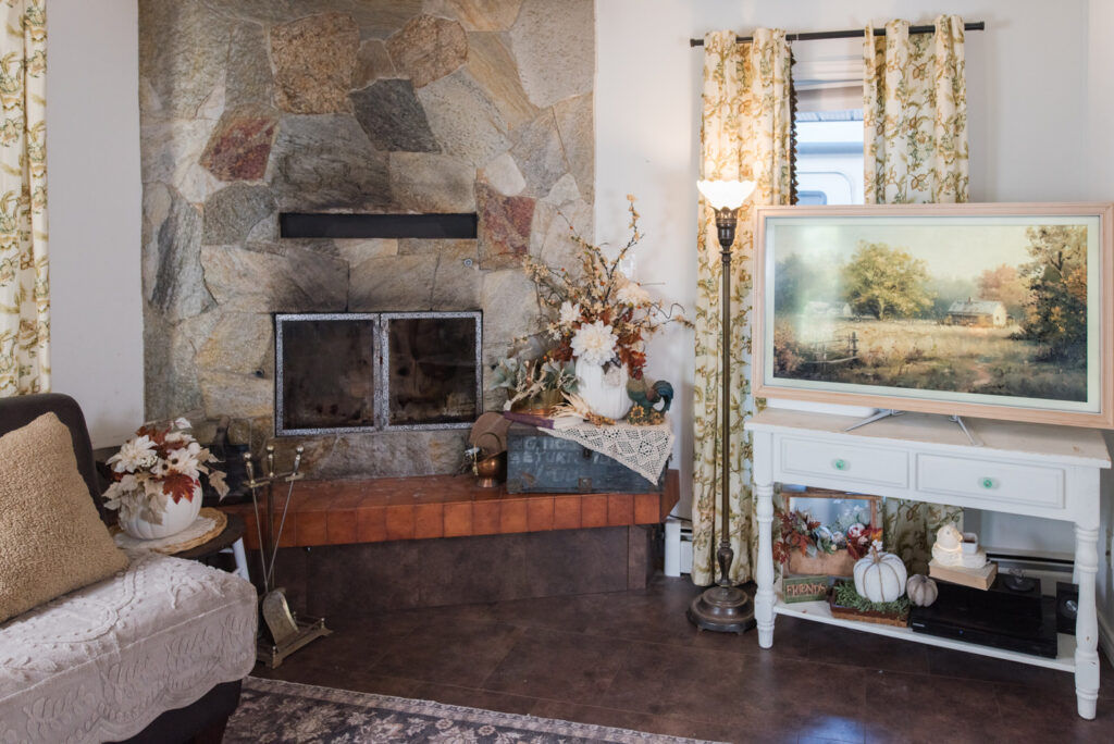 Autumn family room decor with a stone wood-burning fireplace, a vintage lamp, a Frame TV, and a cozy chair