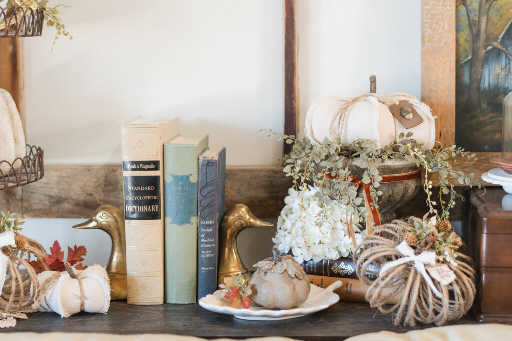Vintage books between brass duck bookends with handmade pumpkins on a dark wood shelf