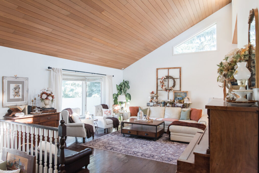 Autumn living room decor with deep brown, rust, and soft green pillows and throws, vintage artwork, and old books
