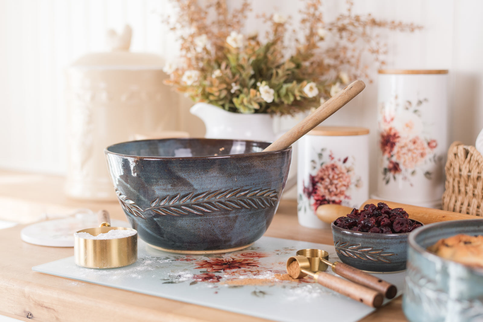 Autumn baking nook with blue pottery and floral canisters with a pitcher and floral stems in the background