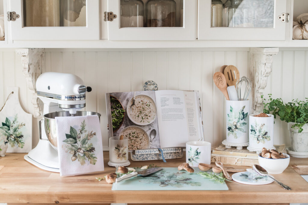 Woodland tea towel draped over a white KitchenAid mixer beside an open cookbook, Woodland canisters and utensil holder, and a bowl of mushrooms